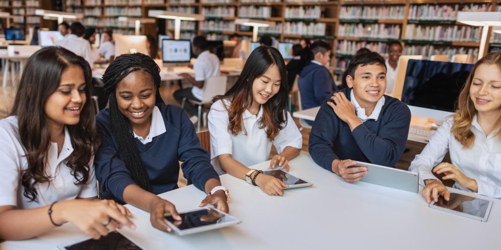 Sekelompok murid sedang berdiskusi menggunakan tablet bersama rekan-rekan di ruang perpustakaan