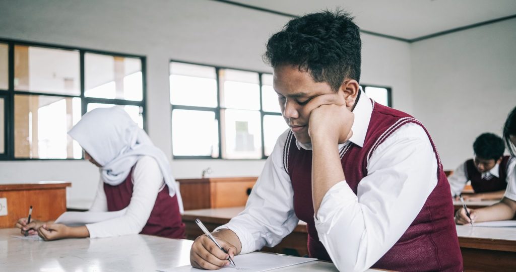 Siswa sekolah sedang fokus mengerjakan soal ujian di ruang kelas untuk persiapan tes bahasa Inggris